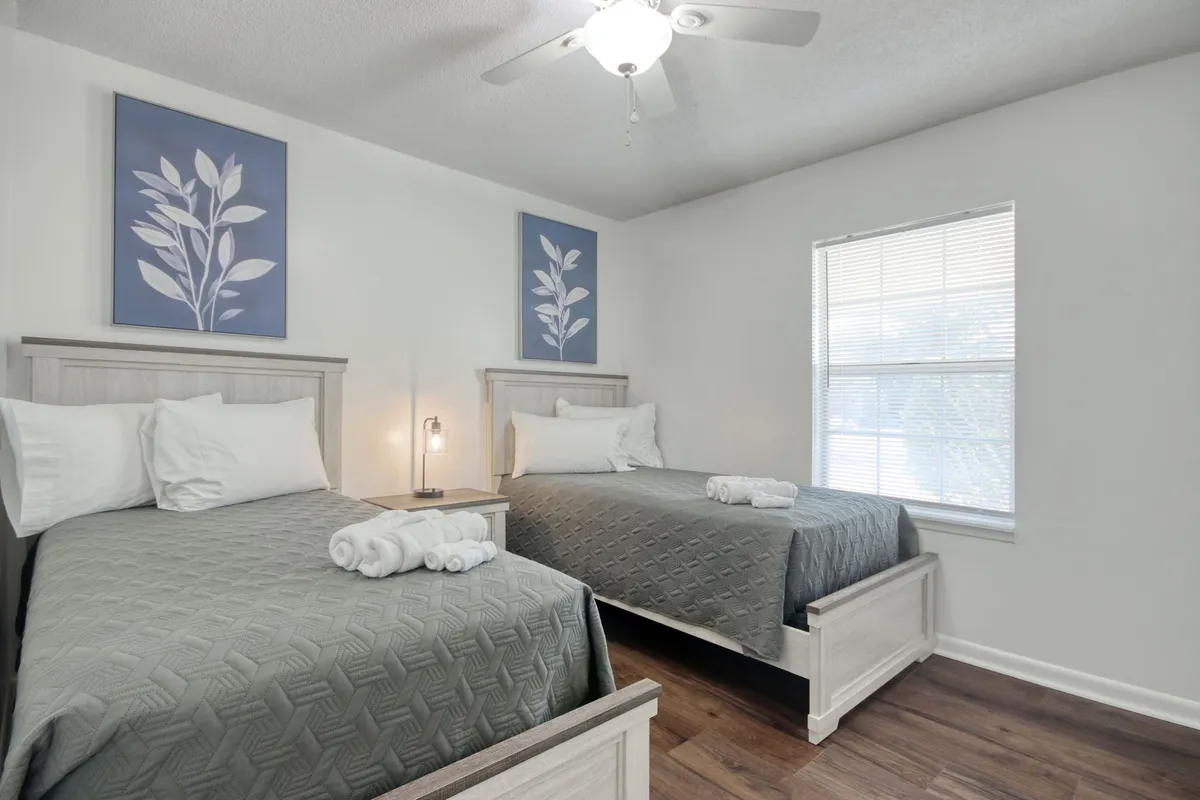 A peaceful bedroom featuring two twin beds with decorative wall art above, a shared nightstand with a lamp between them. The soft lighting and uncluttered style make the room feel inviting and flexible for families or guests.