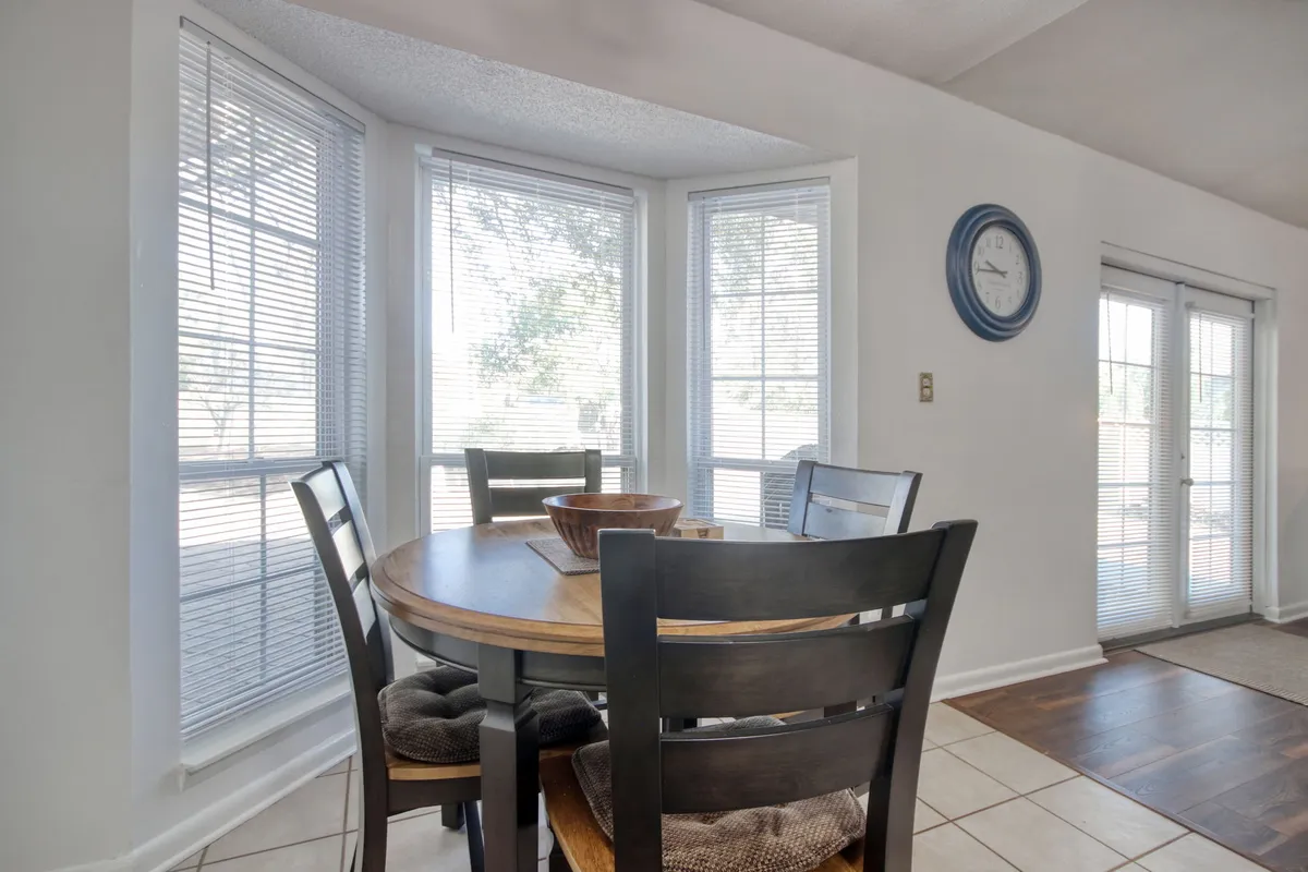 A bright and welcoming dining area featuring a round dining table with wooden chairs positioned by large windows that let in abundant sunlight. The space exudes a sense of warmth and is perfectly set up for shared meals and laughter.
