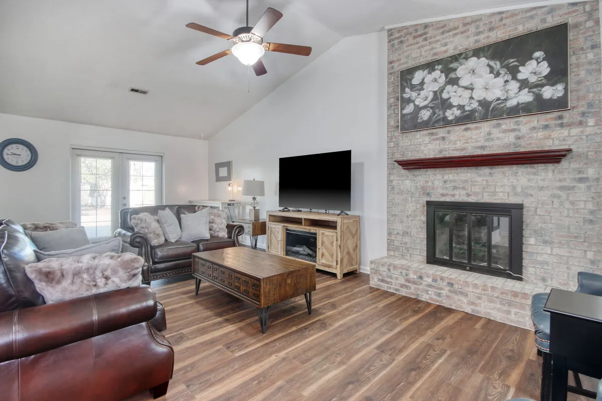 The image showcases a warm, inviting living room with a central brick fireplace, plush sofa set, coffee table, and a TV, all arranged for comfort and relaxation. The space is perfect for family gatherings, cozy evenings, and unwinding after a day at the beach.