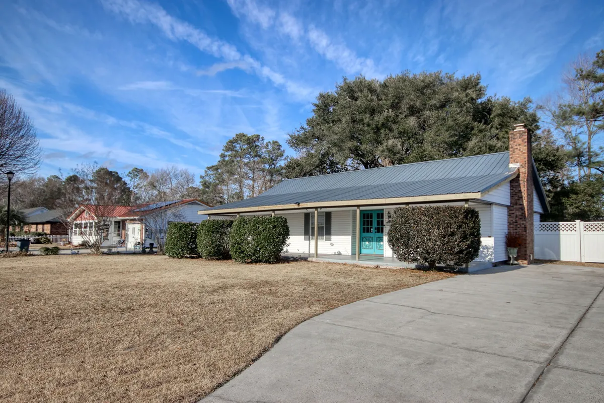 An inviting exterior view highlighting the turquoise front door, lush landscaping, and a driveway leading up to the house. The shot suggests a cheerful atmosphere ideal for family gatherings, children playing, or unwinding after a beach day.