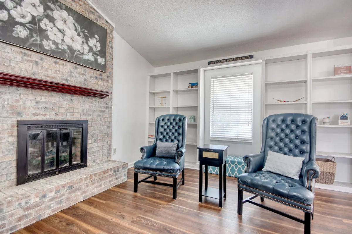 A cozy living room centered around a brick fireplace, flanked by blue leather chairs and shelves adorned with decorative items. The space exudes warmth, ideal for fireside chats, group games, or simply relaxing after a day out.